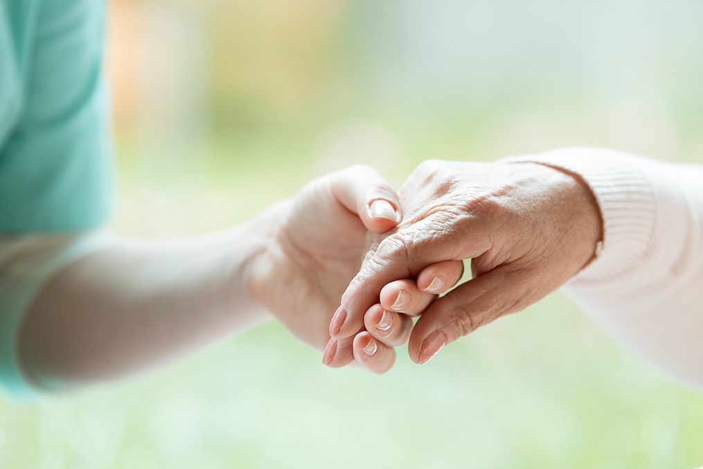 Hand of nurse holding elder woman's in sweater palm
